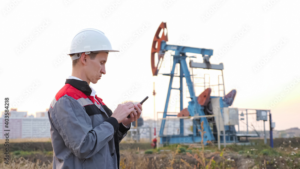 man in a white helmet with a phone against the background of a rocking at an oil well. man in a white helmet with a phone against the background of a rocking at an oil well.
