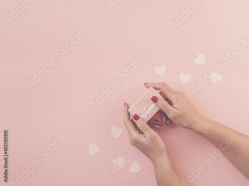 Woman hands holding gift with pink ribbon on pink background, copy space. Flat lay, hands and present box, hearts, top view. Valentine or love, spring holidays, Christmas and birthday concept.