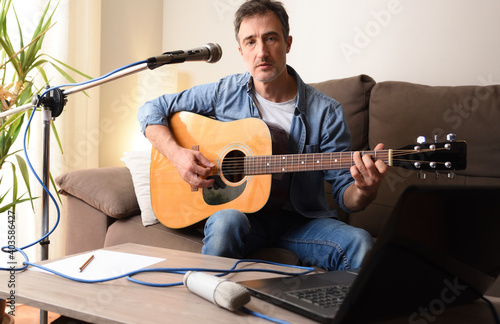 Man playing guitar with microphone and laptop on sofa