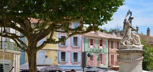 Old town of Orange in Provence-Alpes-Côte d'Azur,  pastel colored old houses with wooden shutters, a maple tree on the left and a medieval fountain on the right
