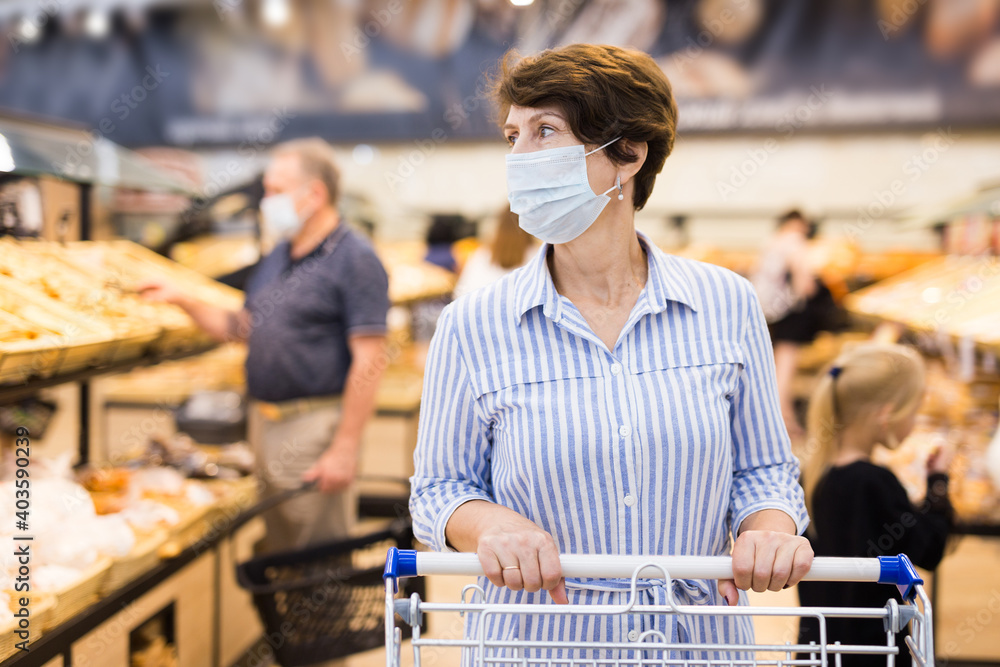 Woman in protective mask with shopping cart in hypermarket