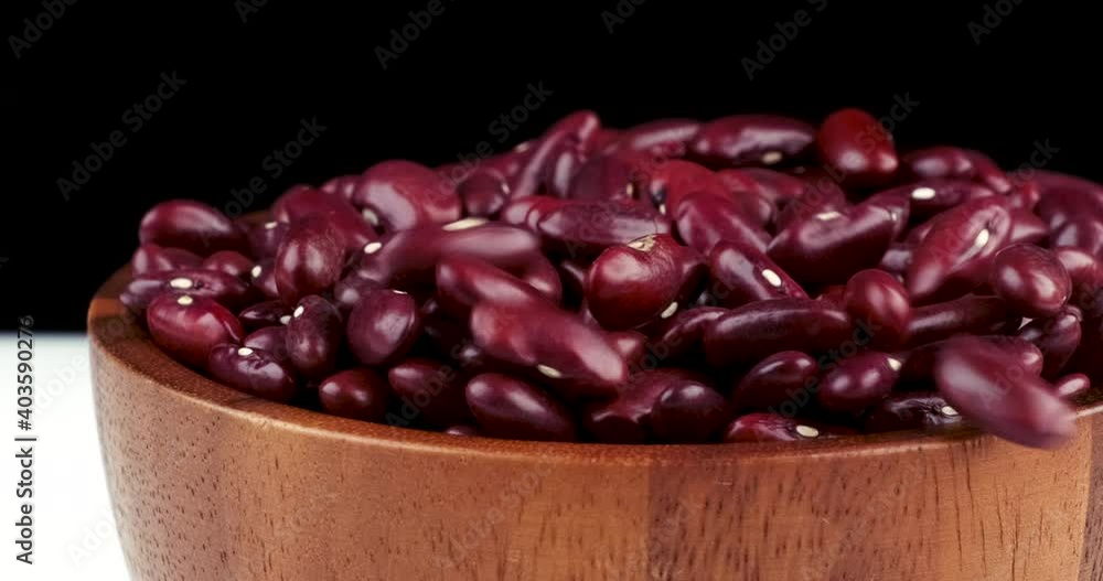 Track shot pouring raw red kidney beans in wooden bowl on black background Track shot pouring raw red kidney beans in wooden bowl on black background