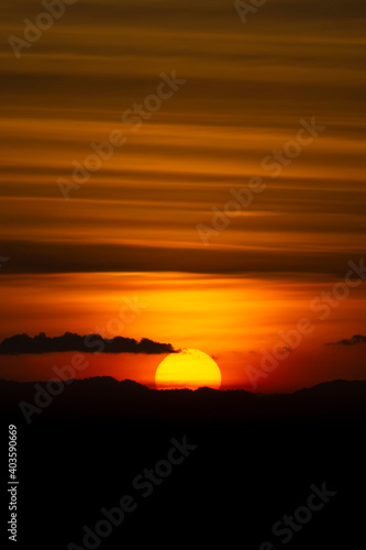 Silhouette mountain with sun and line clouds in sunset sky.