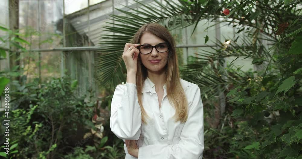Portrait of beautiful young girl in greenhouse smiling and looking at camera. Modern farming, happy youth and profession concept. Elegant young girl in glasses.Scientist inspecting plants. Portrait of beautiful young girl in greenhouse smiling and looking at camera. Modern farming, happy youth and profession concept. Elegant young girl in glasses.Scientist inspecting plants.