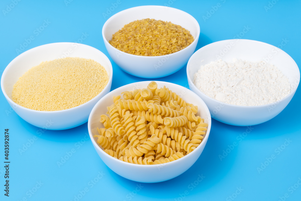 Flour, koukous, bulgur and pasta in bowls on cheerful blue background. Variety of wheat products concept. Flour, koukous, bulgur and pasta in bowls on cheerful blue background. Variety of wheat products concept.
