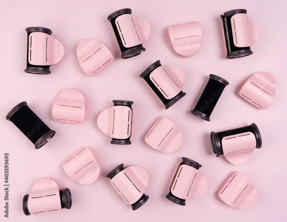 Obraz premium Black hair curlers with pink clothespins on a pink background