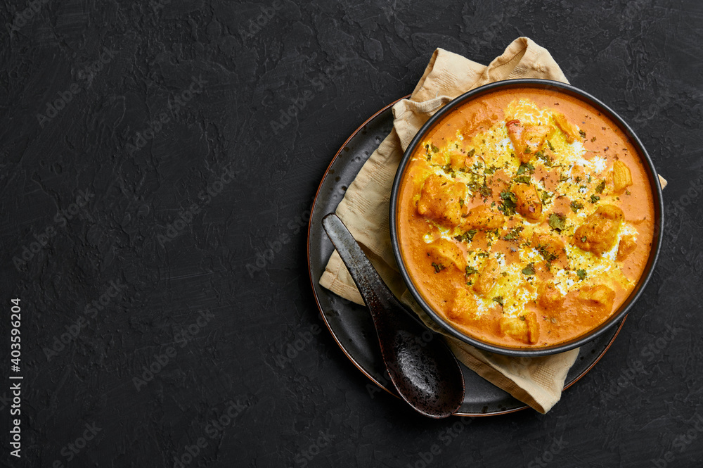 Murgh Makhani or Butter Chicken in black bowl on dark slate table top. Indian Cuisine dish with chicken meat and creamy masala. Asian food and meal. Copy space. Top view Murgh Makhani or Butter Chicken in black bowl on dark slate table top. Indian Cuisine dish with chicken meat and creamy masala. Asian food and meal. Copy space. Top view