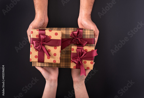 : A person giving two orange color box with black textures in hands along with red color ribbon to a woman.