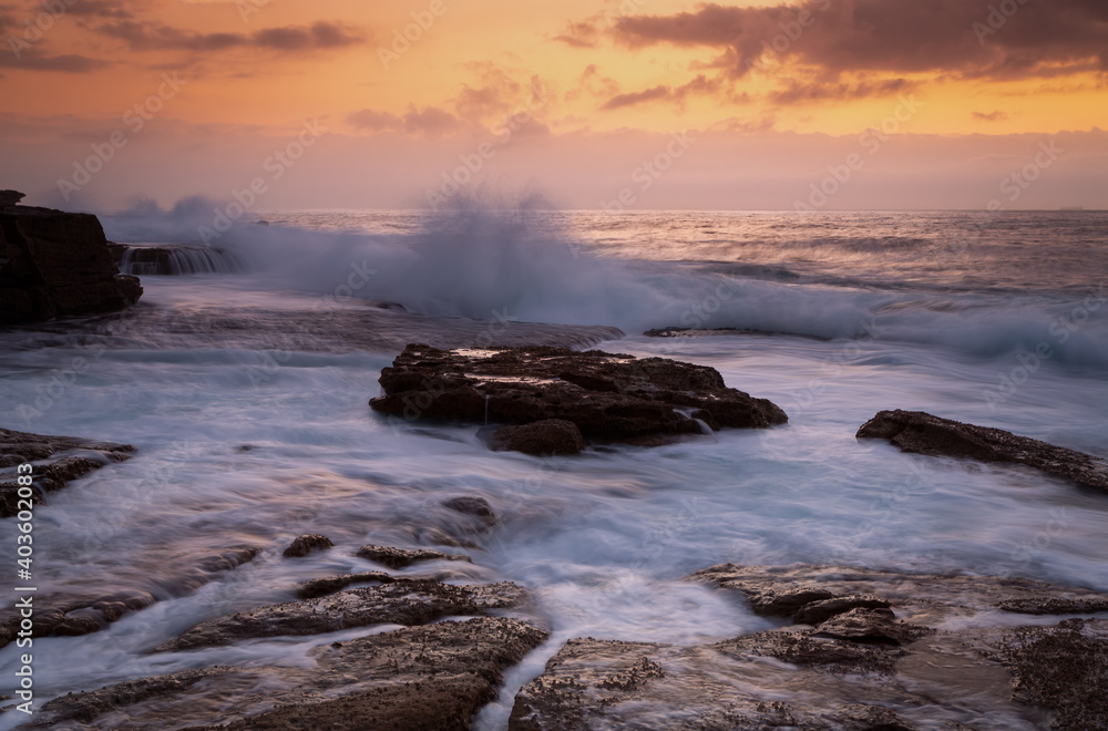 Coastal sunrise waves crashing onto rocks