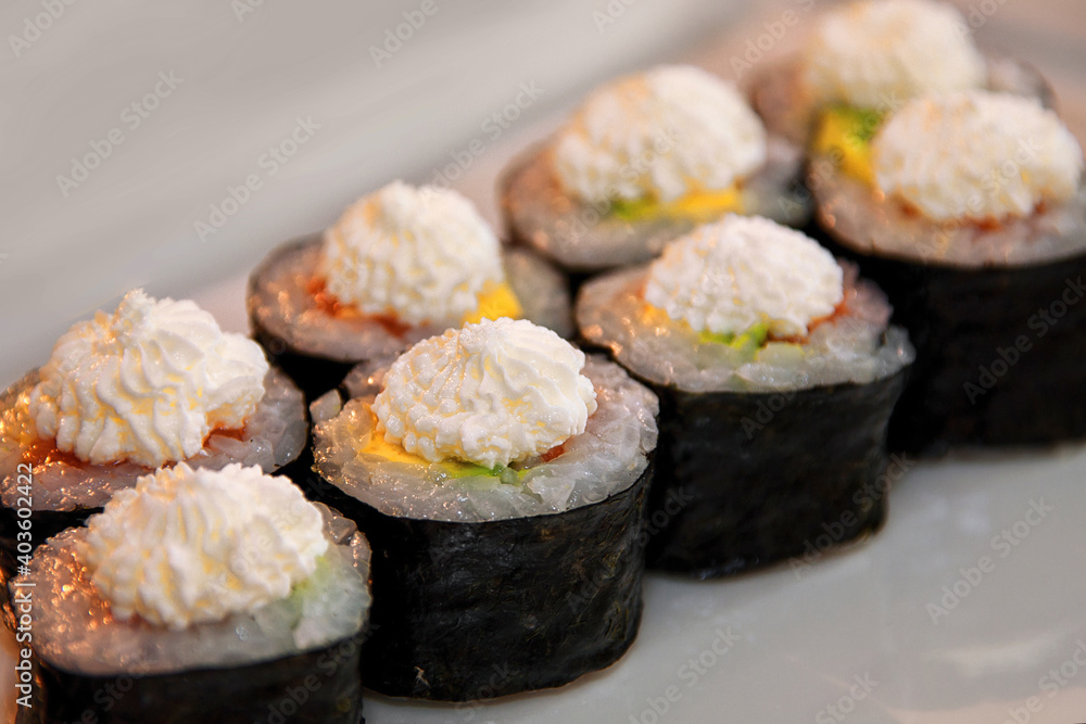 Sushi rolls with fish, caviar, creamy sauce, avocado, on a white plate Sushi rolls with fish, caviar, creamy sauce, avocado, on a white plate