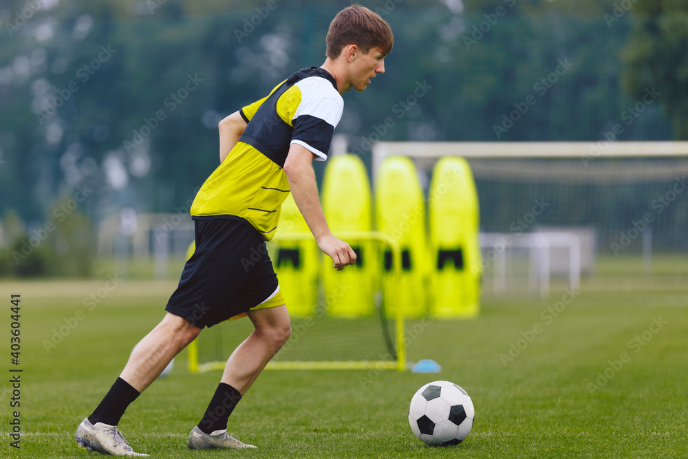 Boys Running Soccer Ball on Training Venue. Young Athlete Practicing Football on Grass Field.  Soccer Wall Mannequin Set and Training Goal in the Background