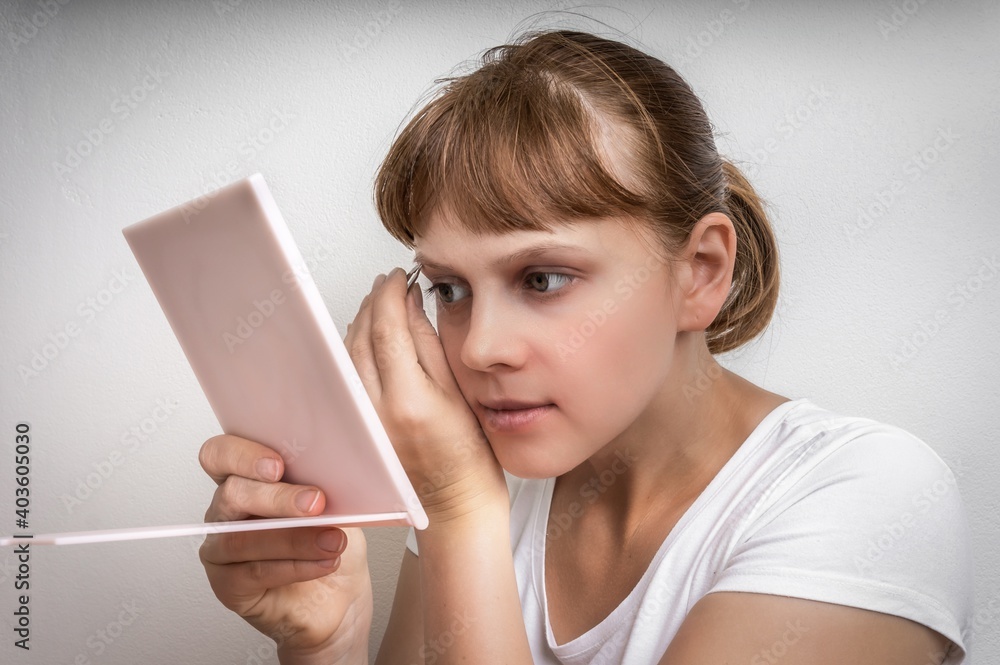 Woman plucking eyebrows with tweezers in front of mirror Woman plucking eyebrows with tweezers in front of mirror