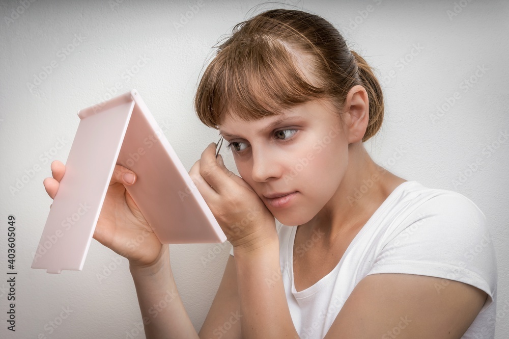 Woman plucking eyebrows with tweezers in front of mirror Woman plucking eyebrows with tweezers in front of mirror