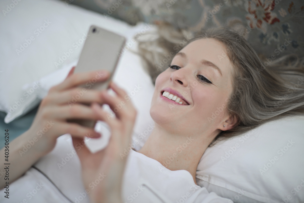 young woman lying on the bed writes with smartphone