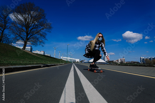 Portrait of a young female in a medical mask with longboard in the city during the quarantine