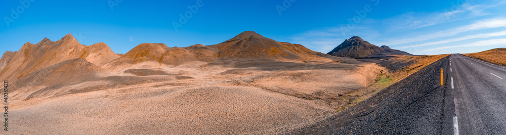 Panoramic view over volcanically active zone in Highlands of Iceland, resembling Martian red planet landscape, with black volcano and road, at summer and blue sky.