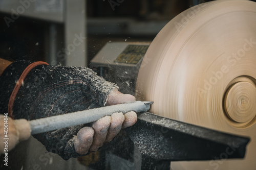 a man in a working apron works on a wood turning lathe. hands hold a chisel. hobby