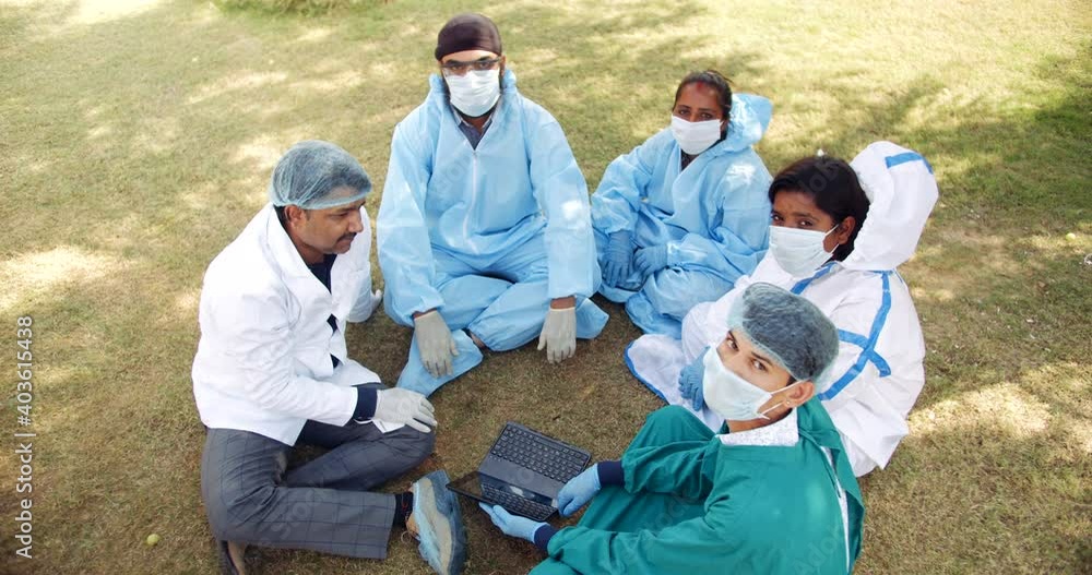 Female and male medical staff taking a break seated on grass outdoors look at camera pov with face expressions wave hands signs gestures point fingers in positive emotions cool attitude Female and male medical staff taking a break seated on grass outdoors look at camera pov with face expressions wave hands signs gestures point fingers in positive emotions cool attitude