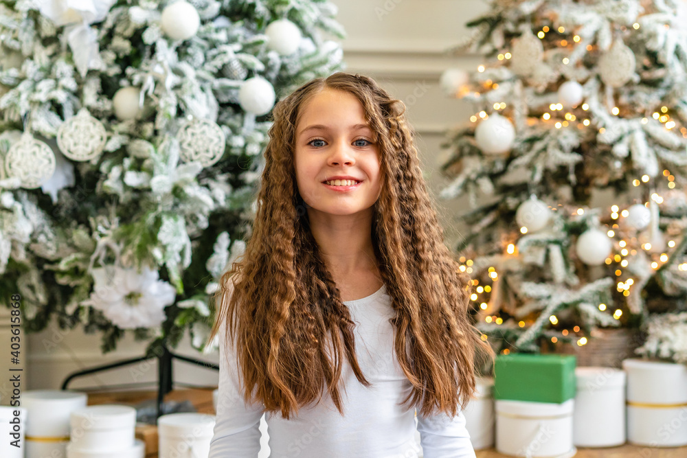 Cute little girl smiles and looks at the camera in a bright studio with Christmas decorations Cute little girl smiles and looks at the camera in a bright studio with Christmas decorations
