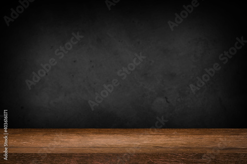 Free space on a wooden table for displaying products with a blurred black wall background.
