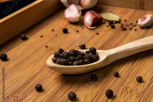 Fototapeta Naklejka Na Ścianę i Meble -  Allspice in a wooden spoon on a wooden background. Garlic and bay leaf. View from above. Seasoning flavoring for meat and food..