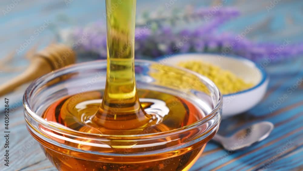Honey pouring, honey dripping from honey dipper over blue wooden background Honey pouring, honey dripping from honey dipper over blue wooden background