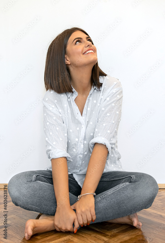 Portrait of young woman looking up. She wears blue dotted shirt and trousers. Woman is sitting on the floor. She looks happy. Portrait of young woman looking up. She wears blue dotted shirt and trousers. Woman is sitting on the floor. She looks happy.