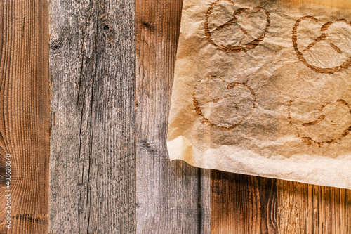 Used baking paper with imprints of baked pretzels on a rustic wooden background. Pretzels are typical German food in Bavaria and at the Oktoberfest. Food background with copy space. Top right corner.