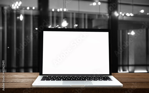 Laptop or notebook with blank screen on wooden table in blurred background in modern home or office, bokeh light and sunlight in the morning.