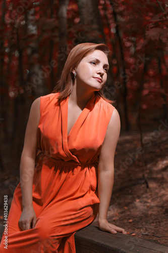 a red-haired woman in red dress posing in an autumn park with harsh sunlight.