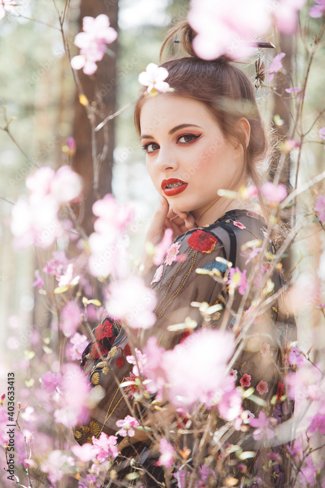 Fototapeta premium Japanese-style girl in a flowering forest among pink flowers in spring