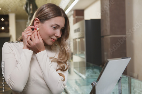 Charming woman looking in the mirror, trying on earrings while shopping at jewelry boutique © mad_production