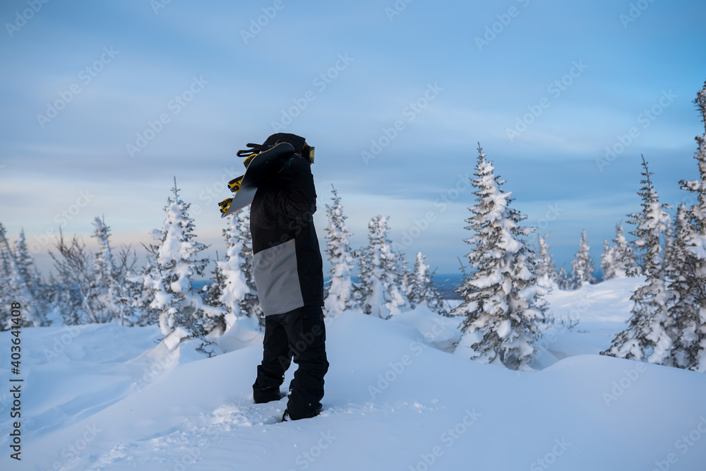 Snowboarder holding his snowboard in hand at the very top of a mountain.
