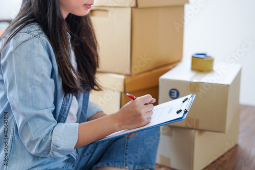 Asian woman checking and packing the carton box prepare to move to new house relocation shipping or check goods package before delivery to customer from online shopping by checklist photo