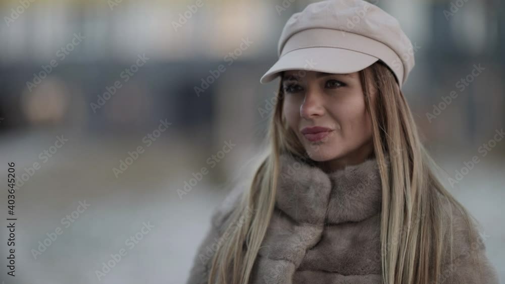 Portrait of a young blonde woman in a sheepskin coat and cap walking and posing on a city street. Winter fashion. Portrait of a young blonde woman in a sheepskin coat and cap walking and posing on a city street. Winter fashion.