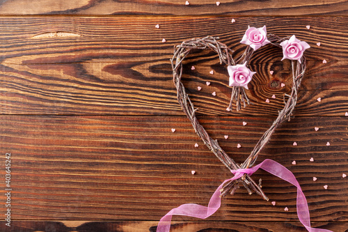 Handmade branches heart with flowers and pink ribbon on wood background for loved one on Valentine day