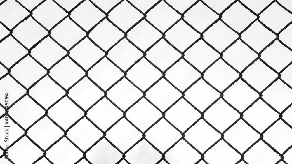 Black metal wire fence with rhombuses in park, view on white sky through it, camera in motion. Background, texture with metal grid and overcast sky in autumn day.