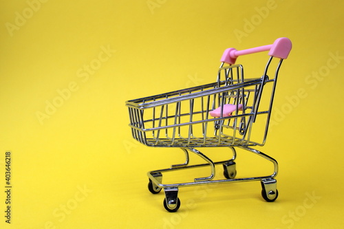 Empty shopping cart stands on yellow background