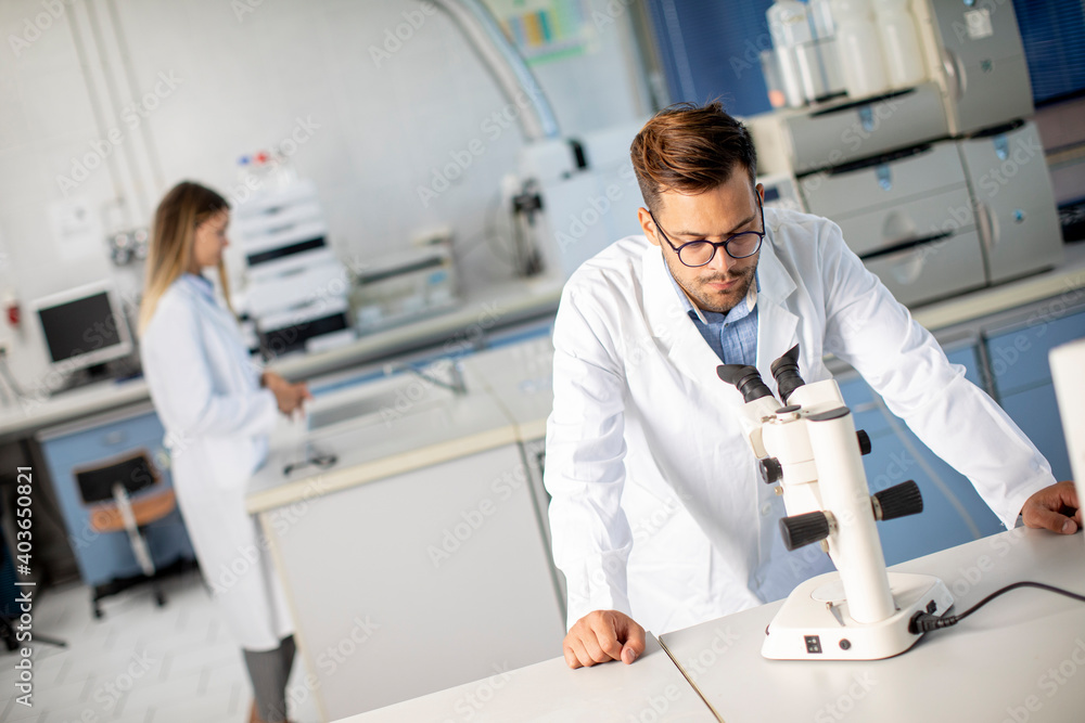 Young scientist in white lab coat working with binocular microscope in the material science lab Young scientist in white lab coat working with binocular microscope in the material science lab