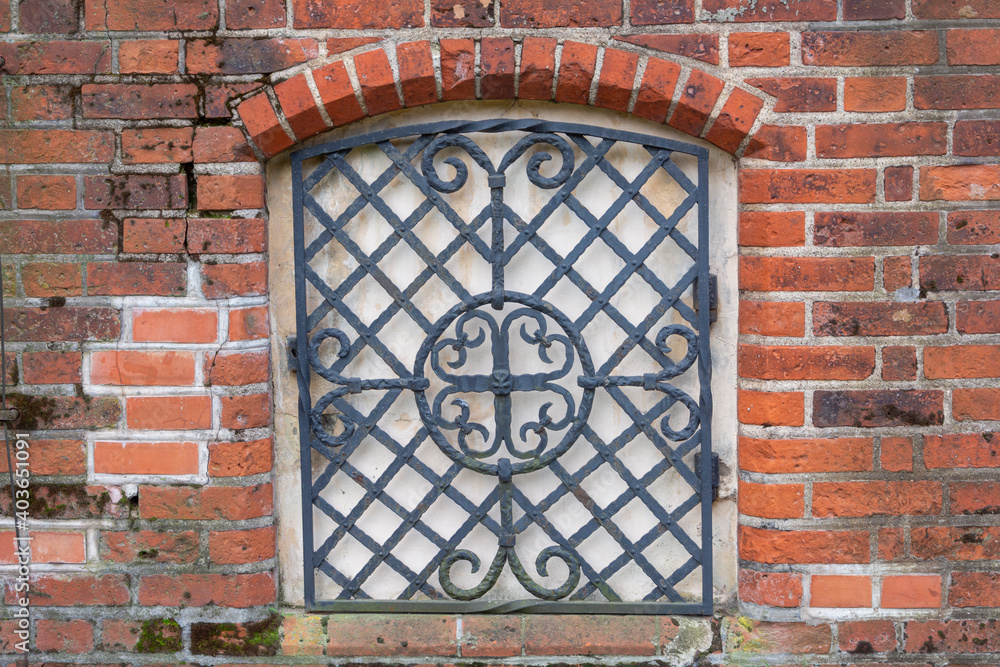 Forged lattice with pattern on closed window of an antique red brick rear. Architecture of medieval Europe Forged lattice with pattern on closed window of an antique red brick rear. Architecture of medieval Europe