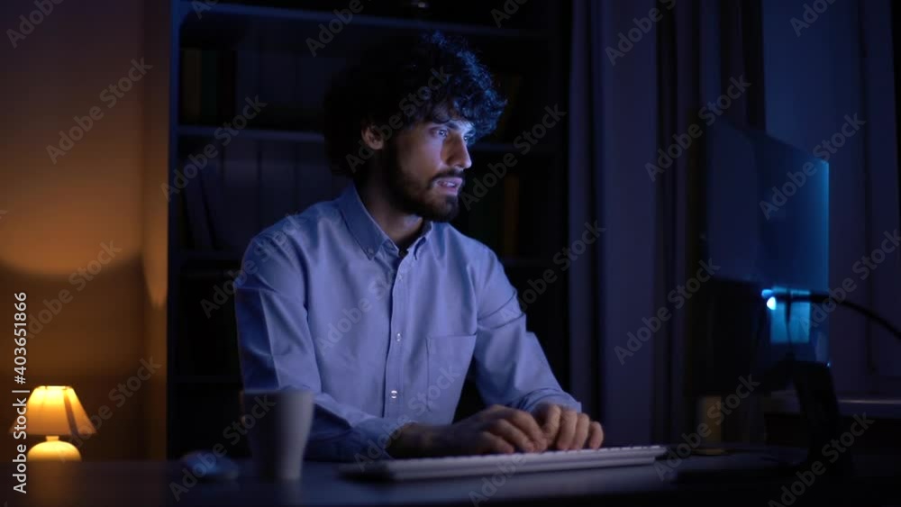 Portrait of young freelancer ends up working at computer at late night. Business man trying to relax in remote workplace at home office in dark living room at nighttime. Shooting in slow motion Portrait of young freelancer ends up working at computer at late night. Business man trying to relax in remote workplace at home office in dark living room at nighttime. Shooting in slow motion