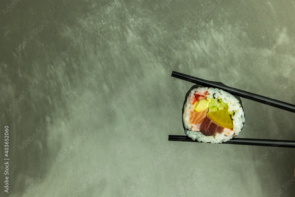 Hand holding sushi roll using chopsticks on gray background Hand holding sushi roll using chopsticks on gray background