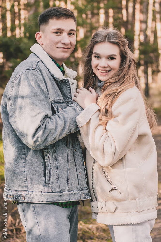couple holding hands smiling and looking into the frame while in a pine forest in winter