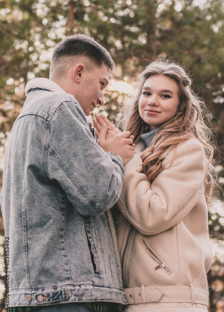 the guy holds the girl's hands and kisses them and the girl smiles while in the pine forest in winter the guy holds the girl's hands and kisses them and the girl smiles while in the pine forest in winter