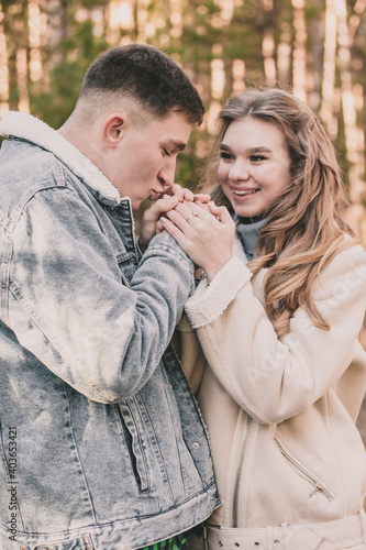 the guy holds the girl's hands and kisses them and the girl smiles while in the pine forest in winter