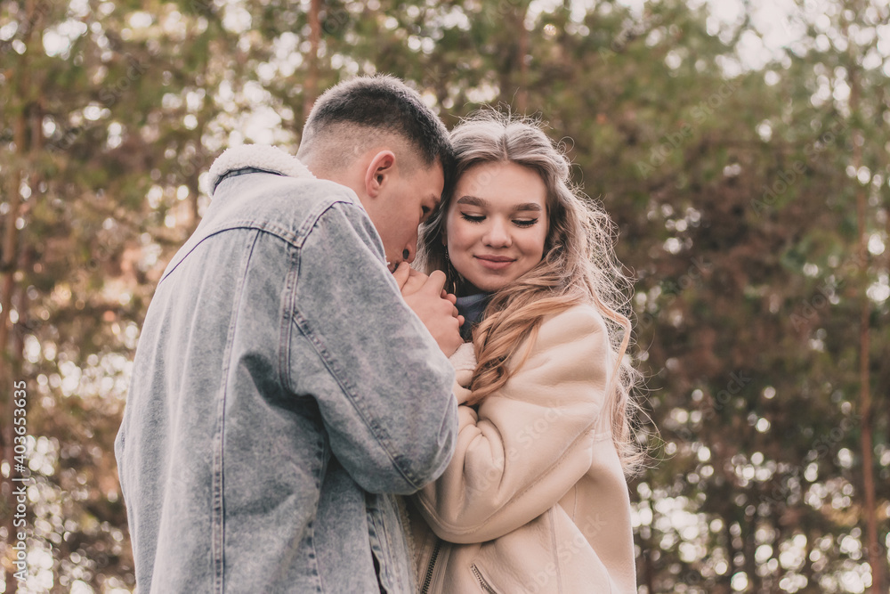 Fototapeta premium the guy holds the girl's hands and kisses them and the girl smiles while in the pine forest in winter