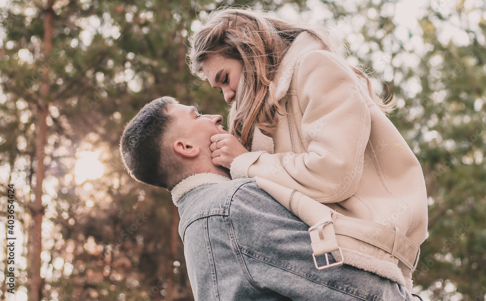 Fototapeta premium The girl jumped into the arms of the guy, holds his face with her hands and smiles in the pine forest