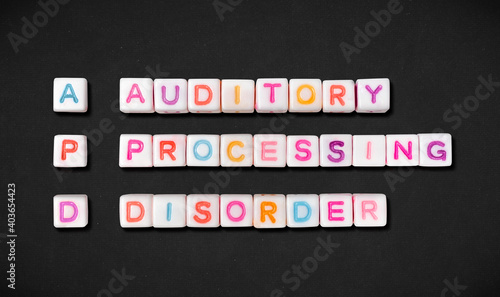 Fotografie Auditory processing disorder and short form APD spelled out in colorful block letters on black textured fabric background