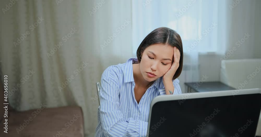 Sleepy young woman brunette with short haircut looks at black laptop display listening to online lecture in room staying home Sleepy young woman brunette with short haircut looks at black laptop display listening to online lecture in room staying home