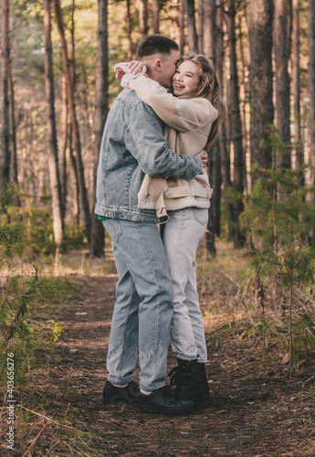  the guy hugs the girl tightly and kisses her on the cheek while in the pine forest